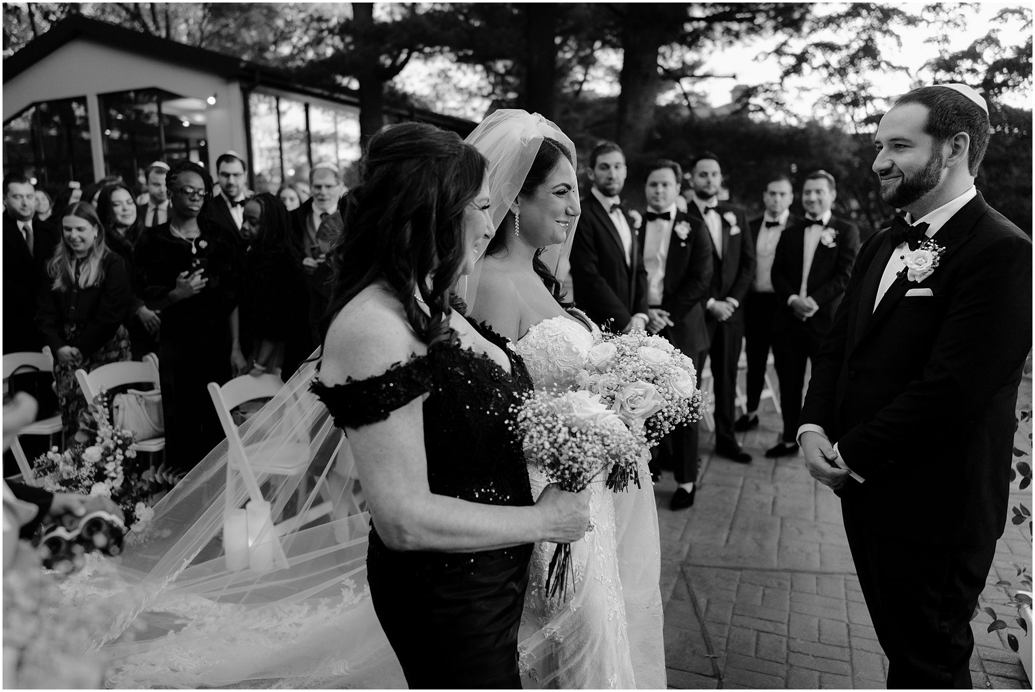 mother walks bride to groom during Jewish wedding ceremony on the patio at Tappan Hill Mansion