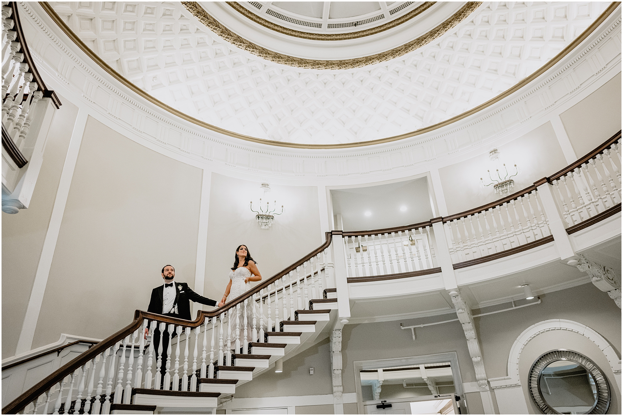 bride and groom hold hands walking down white and brown staircase inside Tappan Hill Mansion