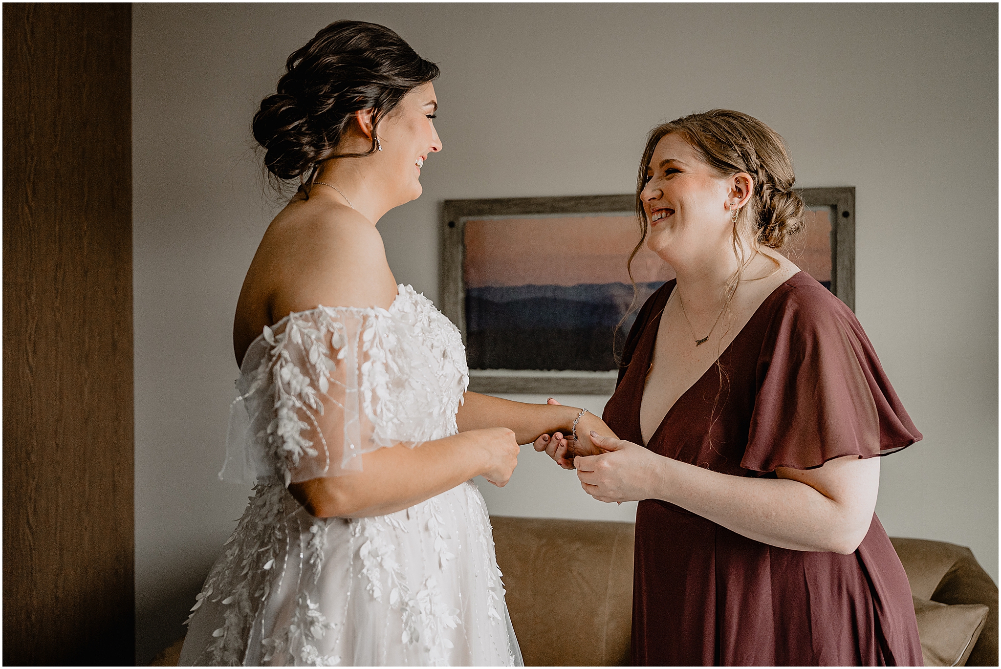 bridesmaid laughs with bride helping her with jewelry during prep at New Jersey hotel