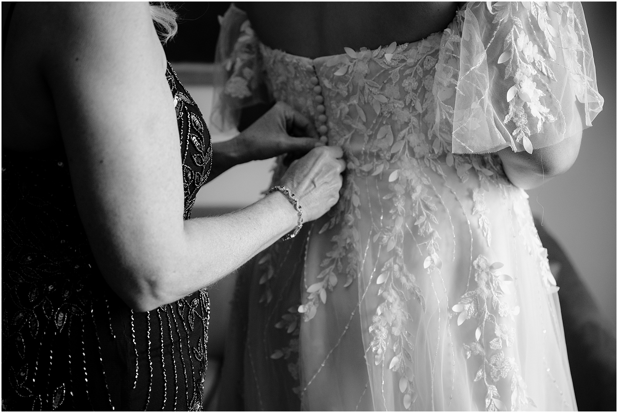 woman buttons up wedding gown for bride during prep in New Jersey hotel