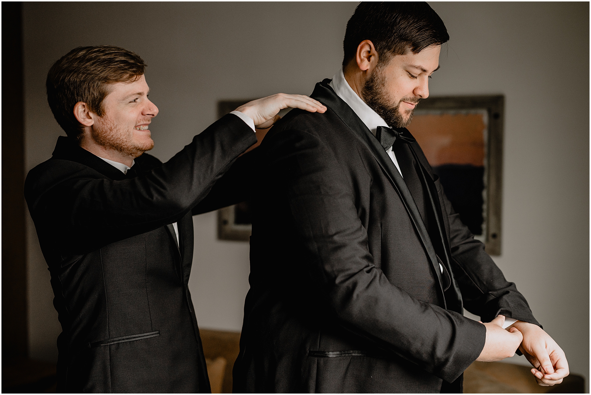 groomsman brushes off top of jacket for groom during prep in Andover NJ hotel