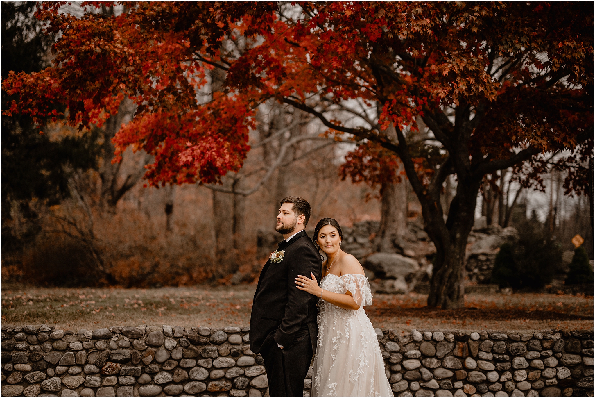 bride stands behind groom in front of stone wall at the Perona Farms Reserve