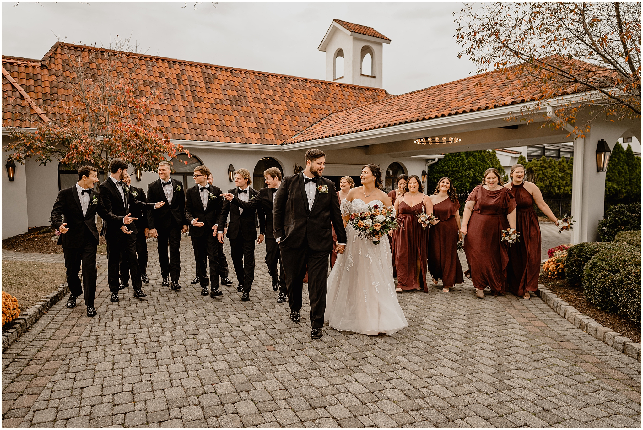 bride and groom walk outside the Perona Farms Reserve with wedding party in burgundy gowns and black suits