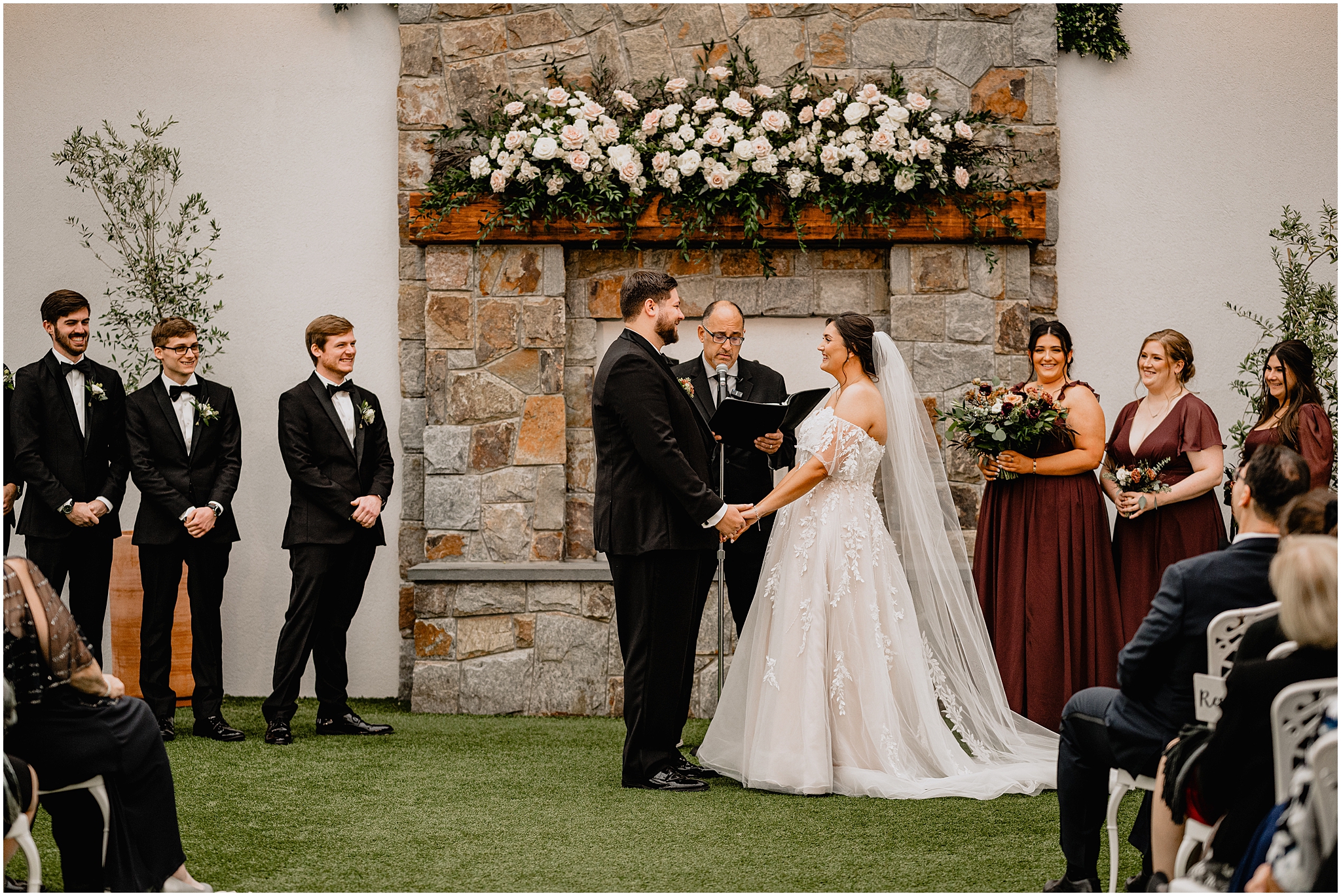 newlyweds hold hands in front of stone fireplace during wedding ceremony in the atrium at Perona Farms Reserve