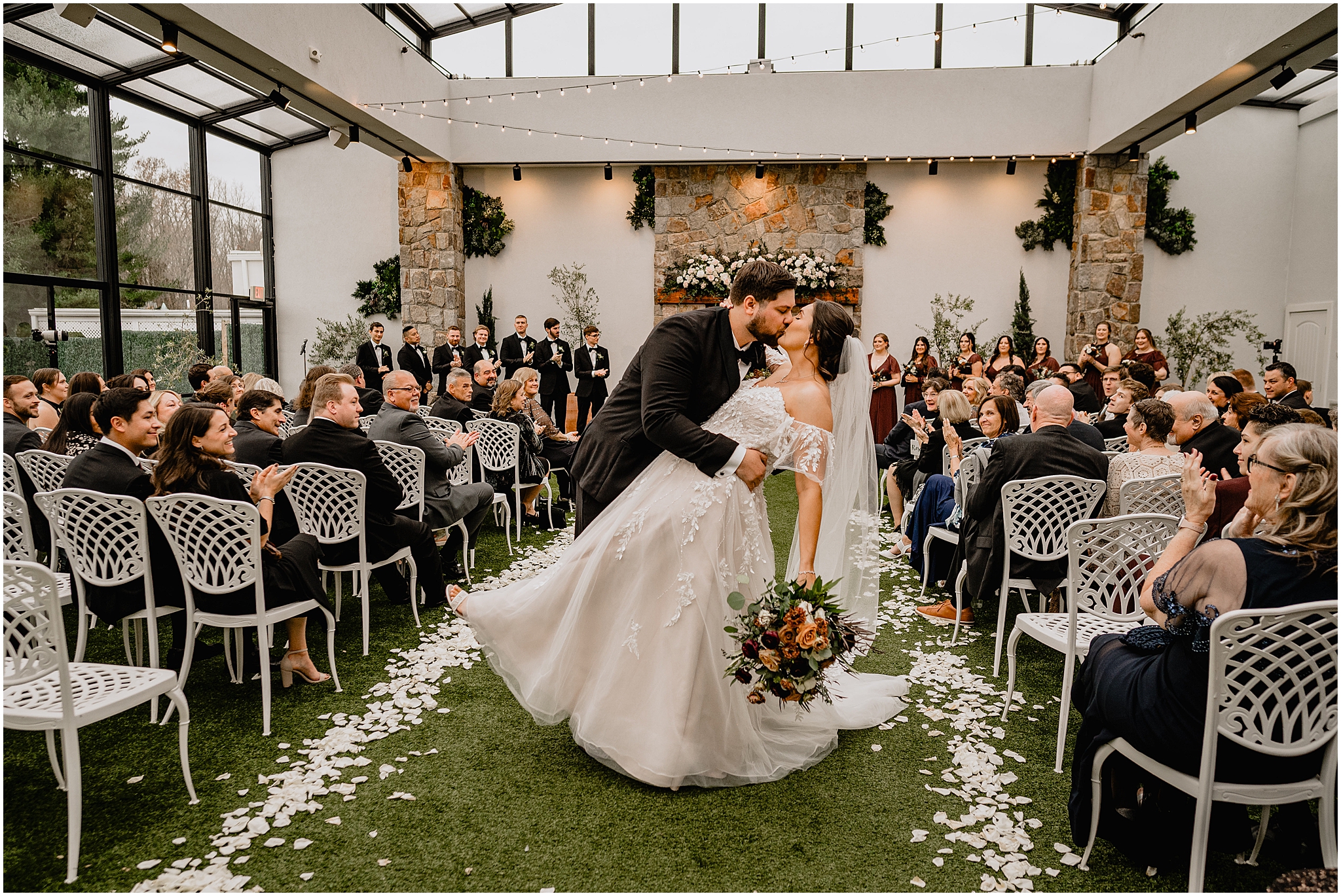 groom dips bride kissing her in the aisle during wedding ceremony in the atrium at Perona Farms Reserve