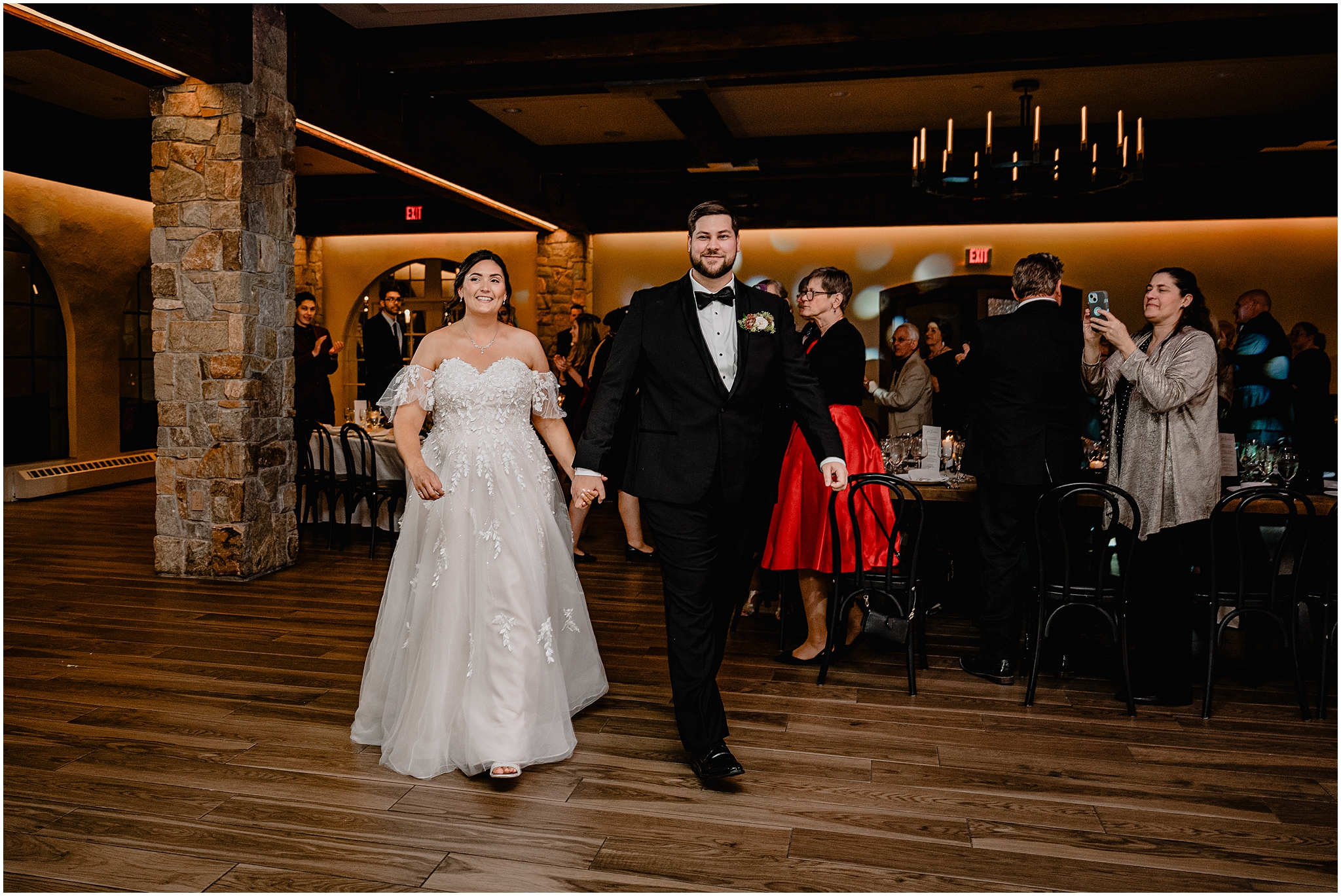 bride and groom hold hands walking across dance floor in ballroom 