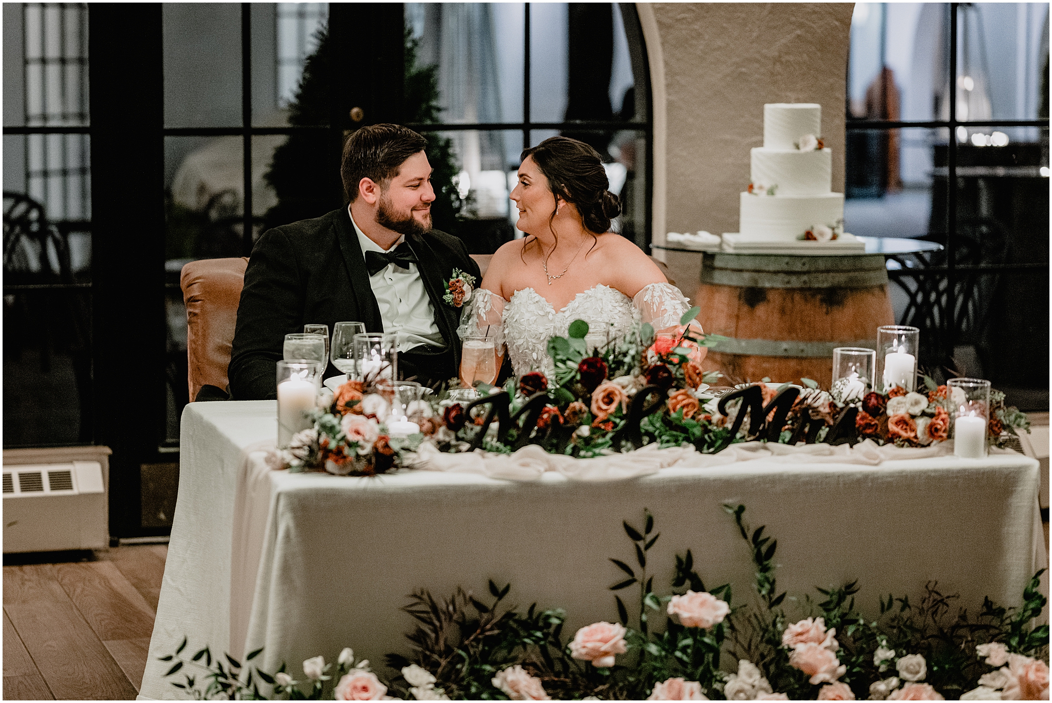 bride and groom sit at sweetheart table with spray of pink roses in front of table at Andover NJ wedding reception