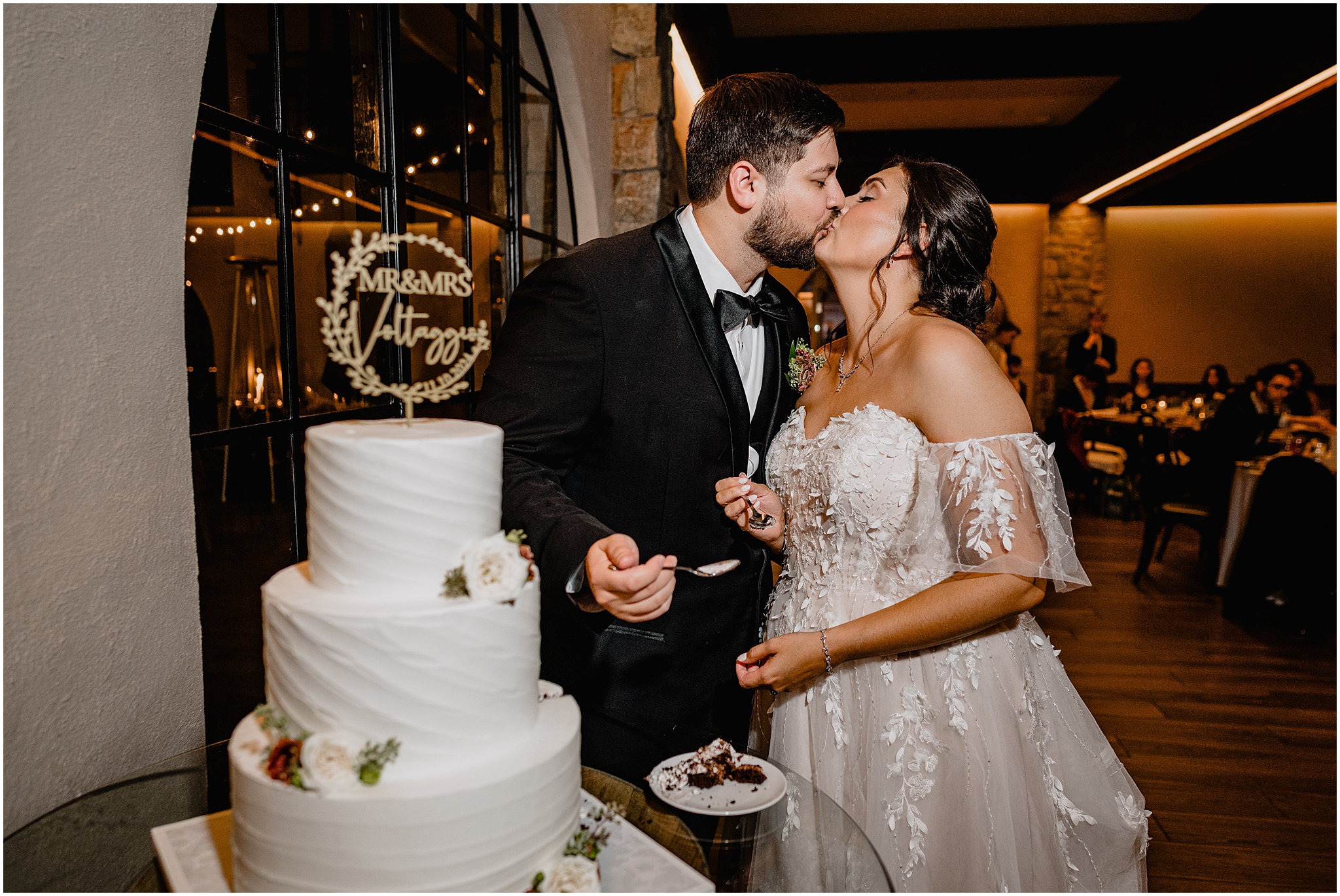 bride and groom kiss by tiered wedding cake with custom topper during Andover NJ wedding reception