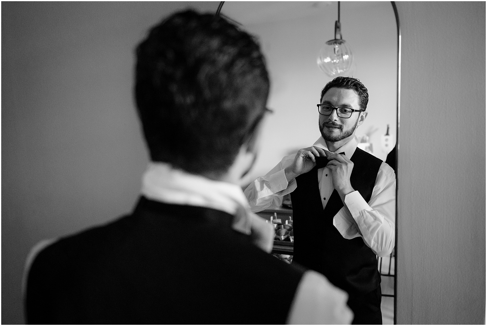 groom adjusts bow tie in mirror during prep for Philadelphia wedding
