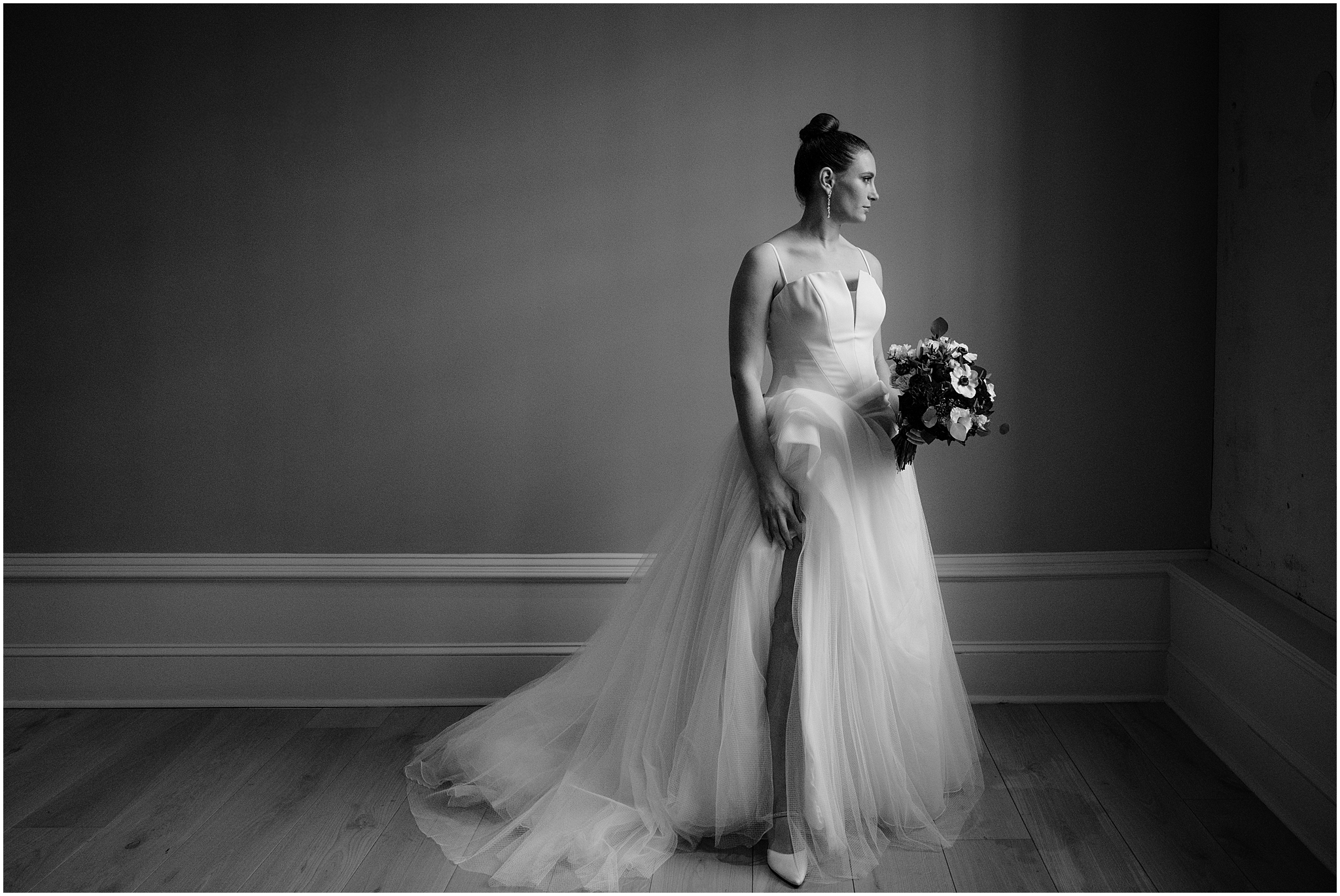 dramatic portrait of bride in strapless wedding gown with bouquet of flowers looking at window
