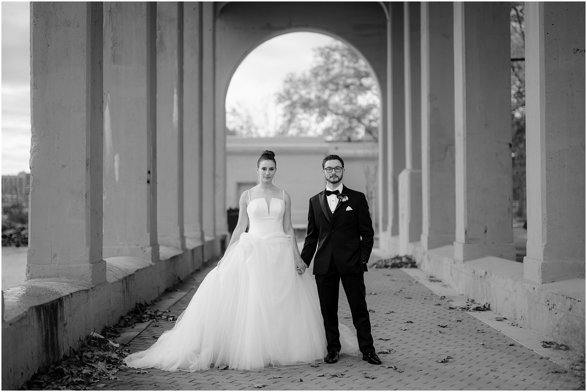 bride and groom hold hands under archways at Penn Landing along the Delaware River