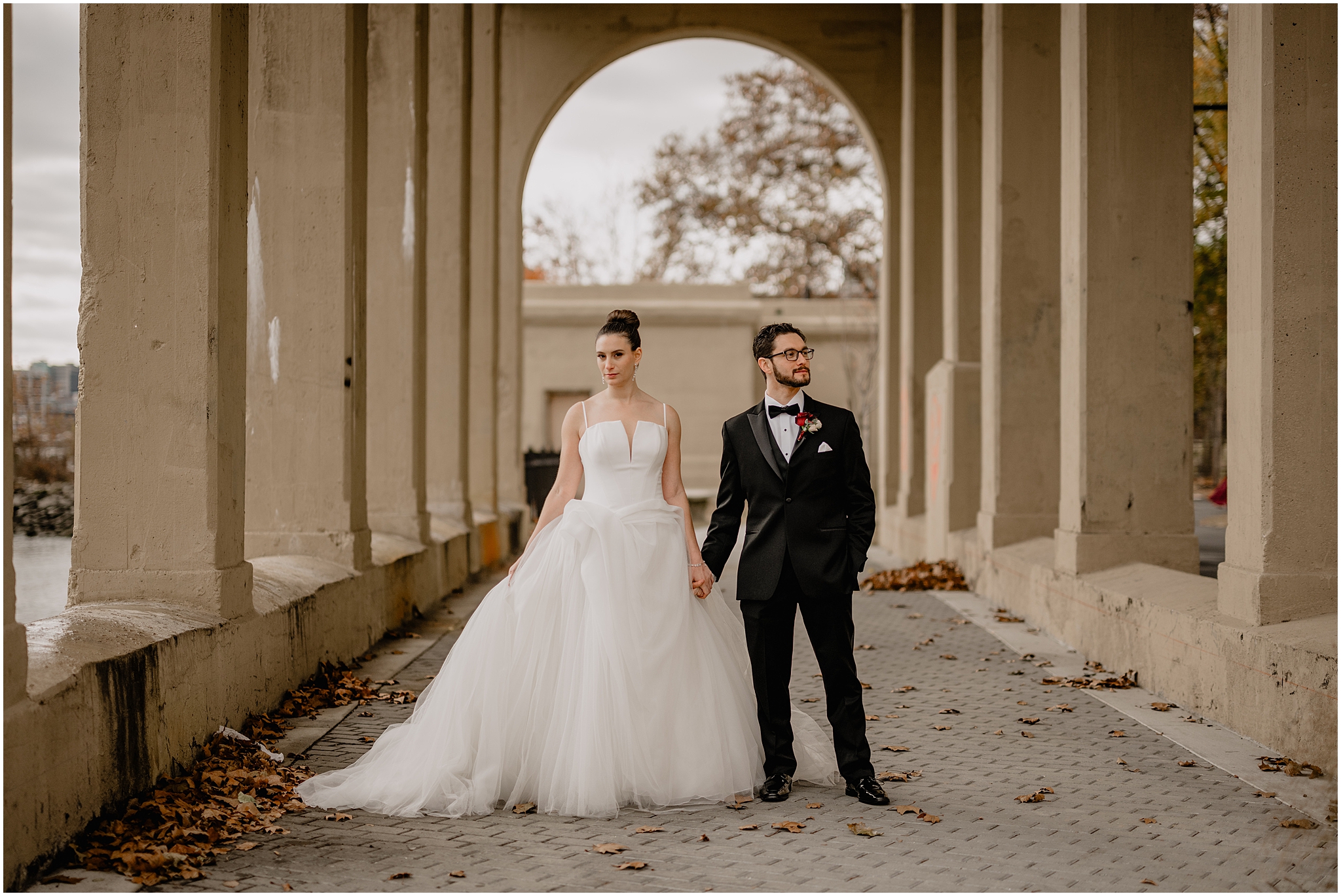 bride and groom hold hands under archways at Penn Landing along the Delaware River