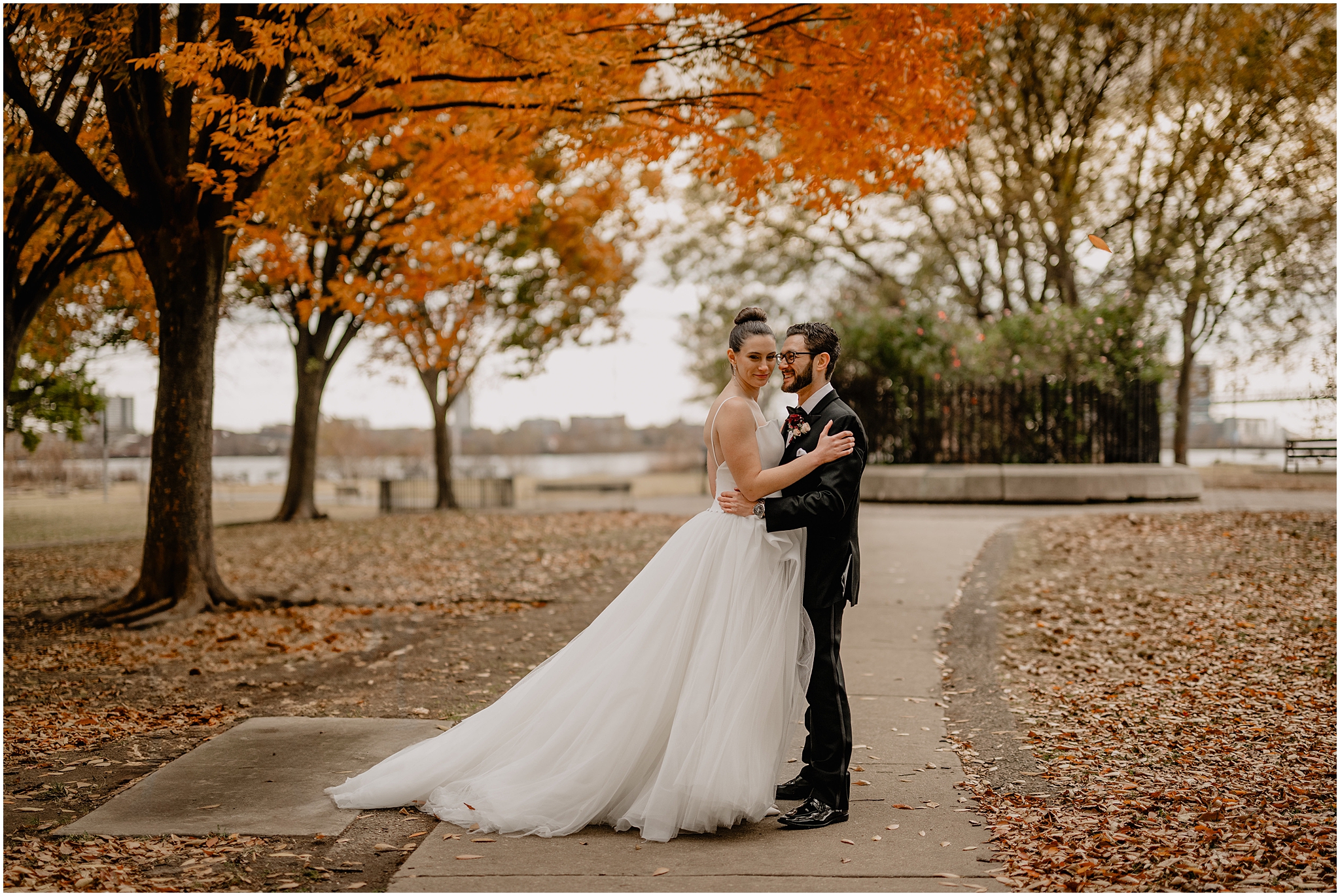 bride and groom hug on the sidewalk under trees with orange leaves in Philadelphia PA