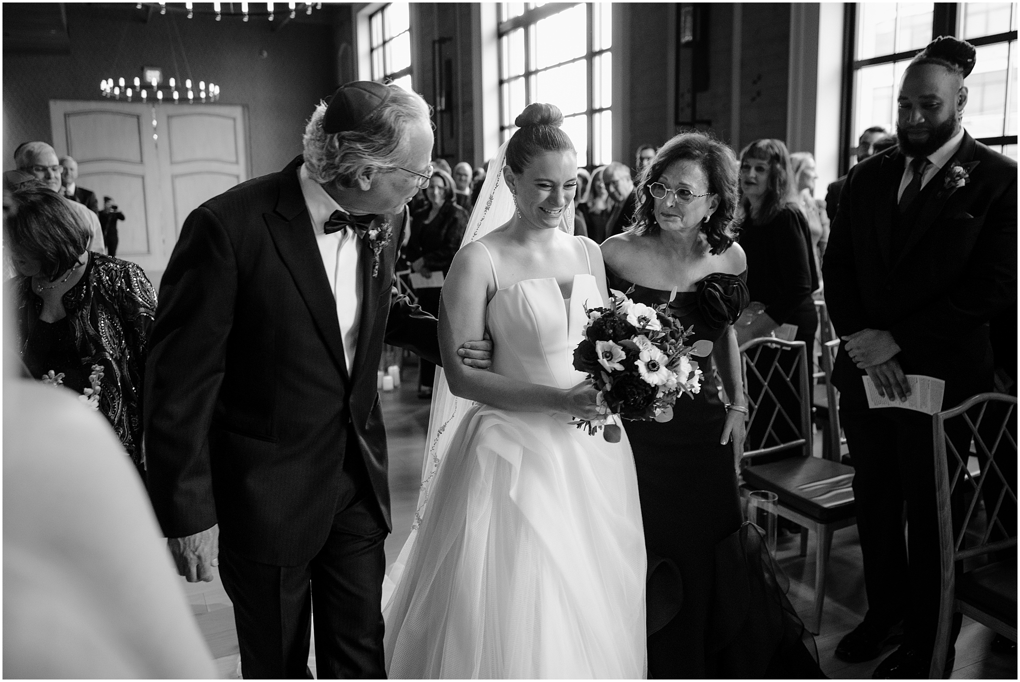 parents smile at daughter walking down the aisle for Jewish wedding ceremony inside Cescaphe's Switch House in Philadelphia PA