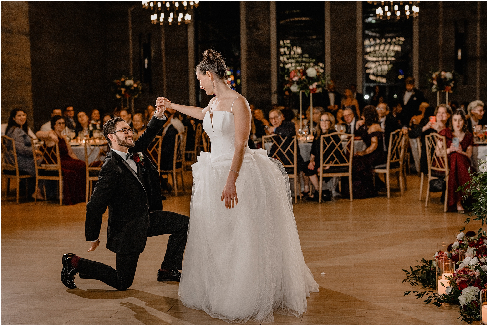 groom kneels next to bride during first dance atPhiladelphia PA wedding reception in the ballroom