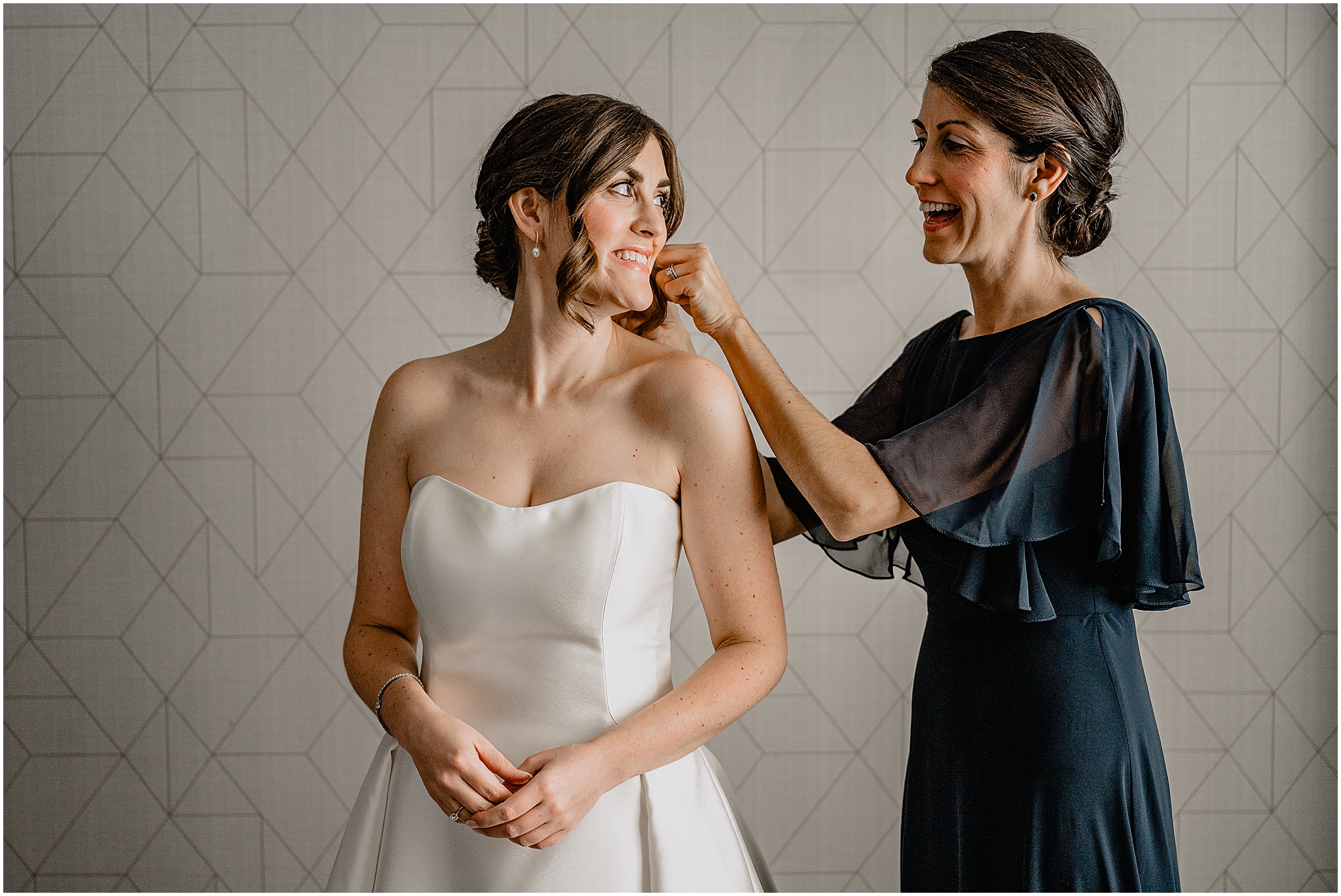 woman in navy blue gown helps bride with earrings during prep in Hudson Valley hotel
