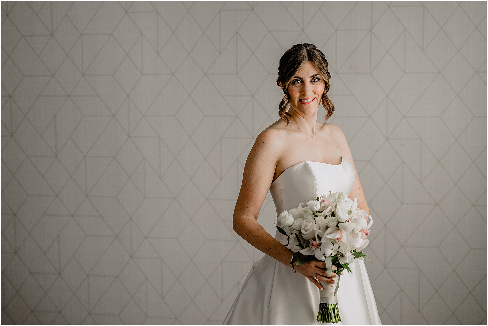 bride holds bouquet of white flowers in front of geometric wall in Hudson Valley hotel