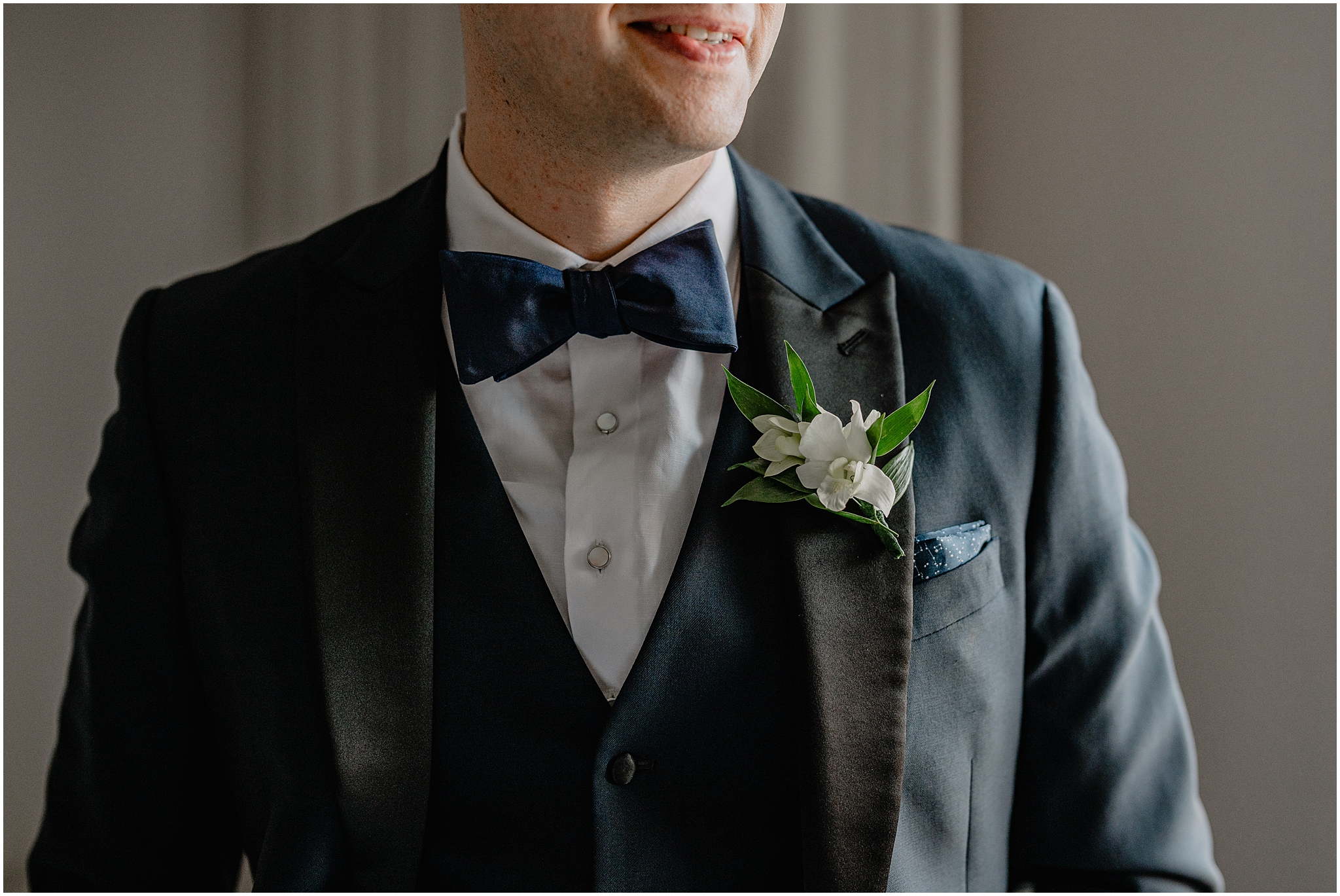 closeup of groom's navy tie with black suit and white floral boutonnière 