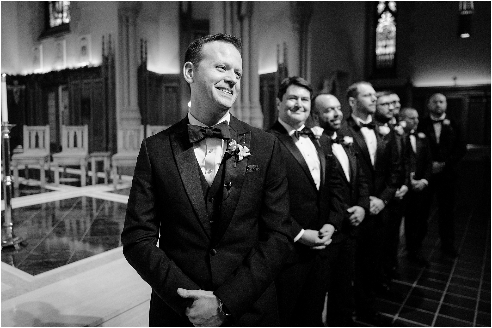 groom grins looking down aisle inside New York church during traditional wedding ceremony