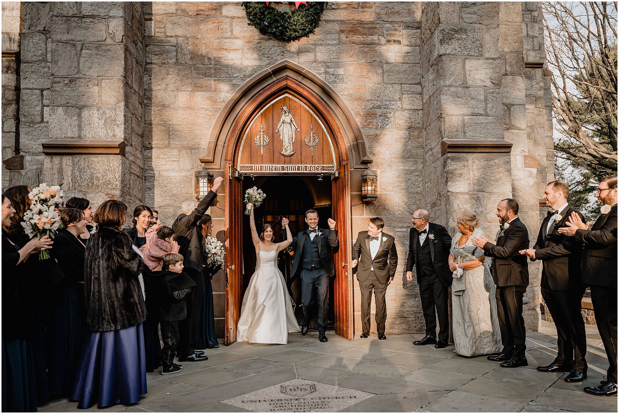 newlyweds walk through door of New York church with wedding guests cheering 