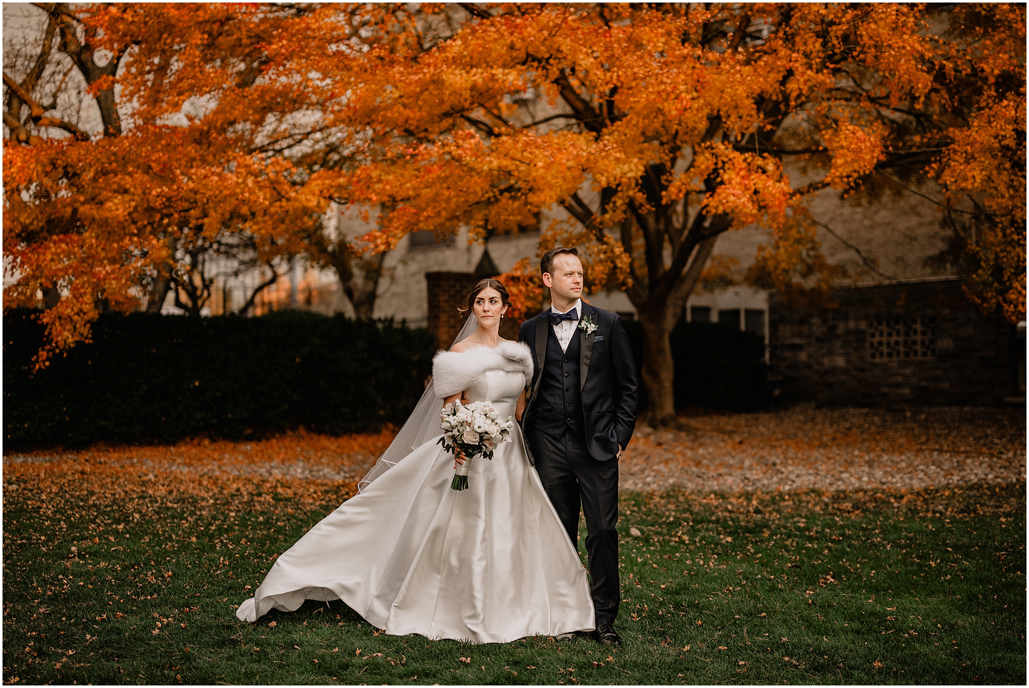 bride and groom pose in front of trees with orange leaves in the Hudson Valley