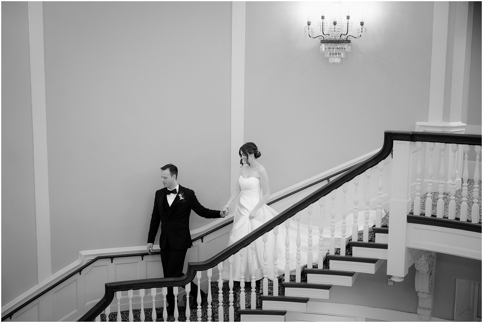 groom leads bride down carpeted staircase inside Tappan Hill Mansion