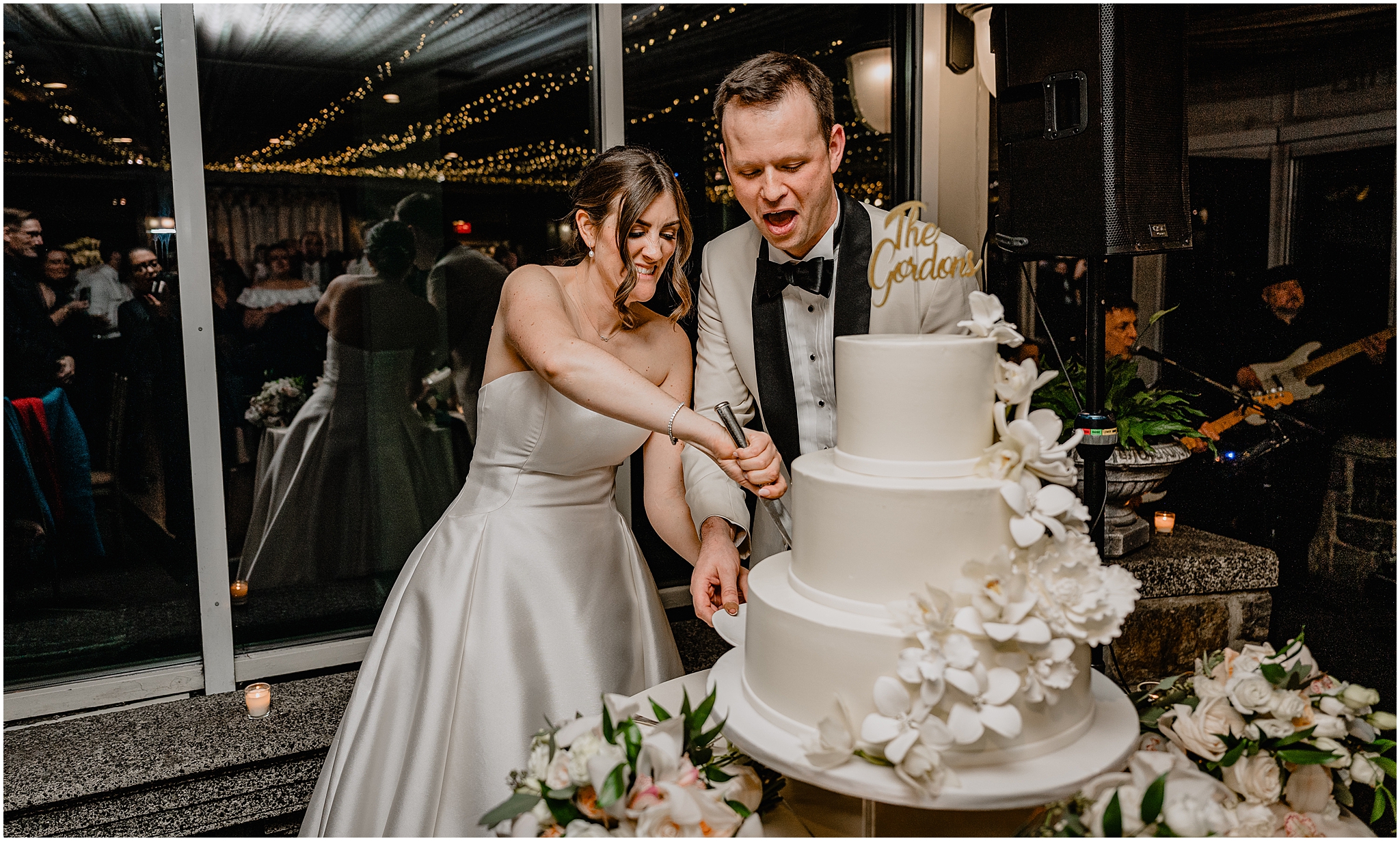 newlyweds cut tiered wedding cake with white flowers around the side of the cake at Tarrytown NY wedding reception