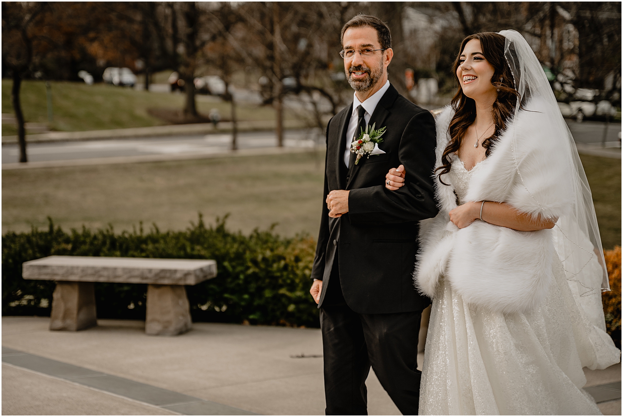 father escorts winter bride with fur around shoulders across parking lot outside the church 
