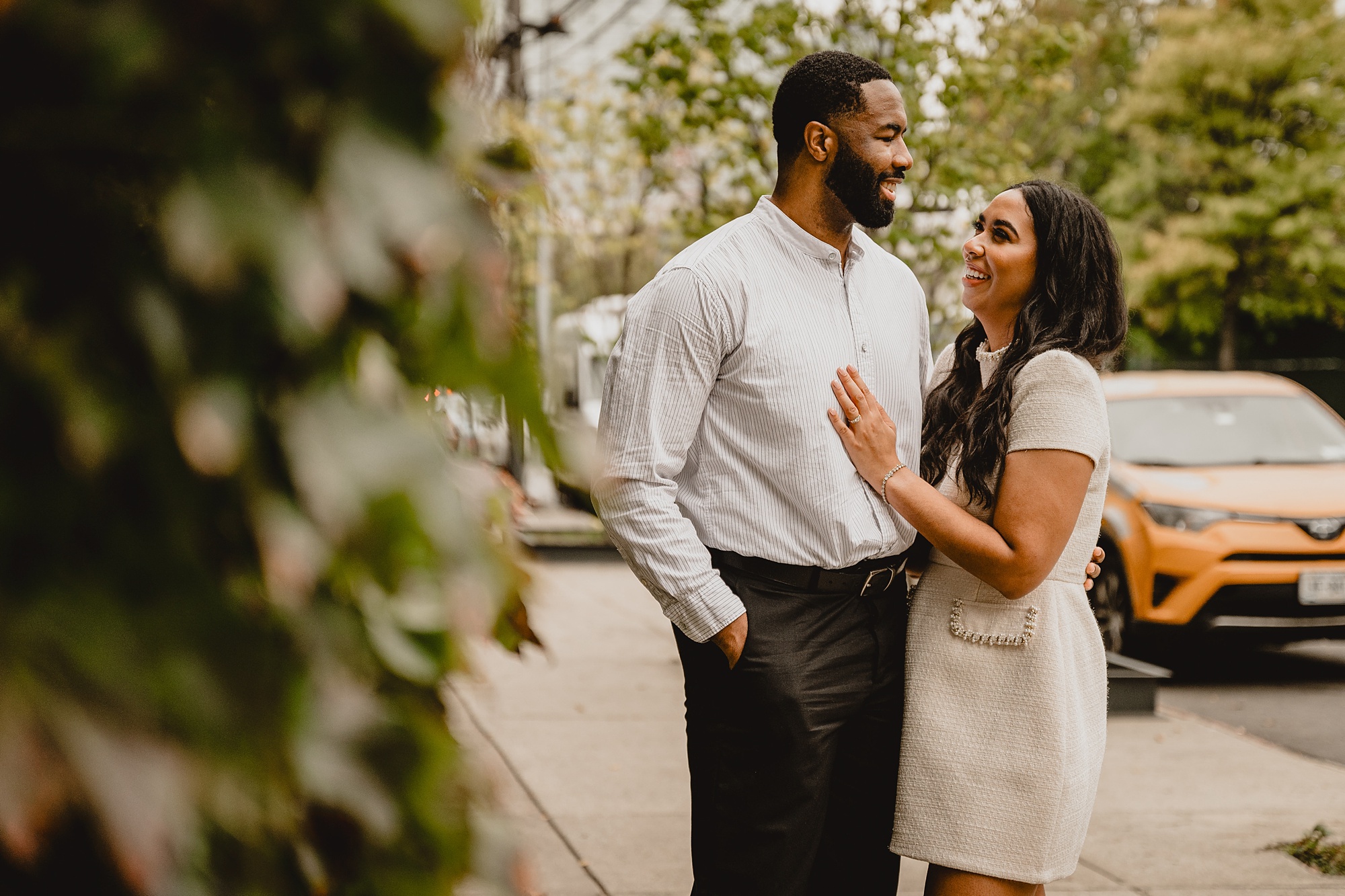 woman lays hand on man's chest standing outside The Foundry for their Long Island Engagement Session.