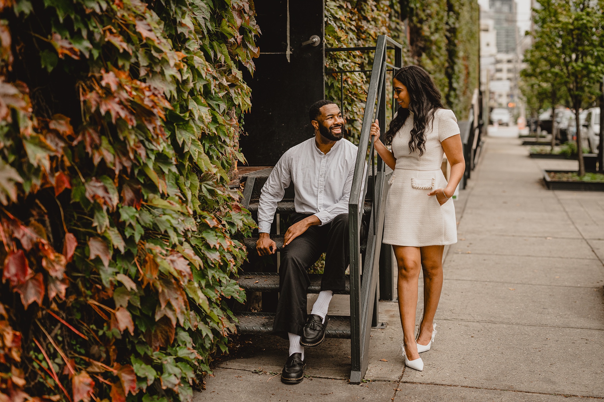 man sits on step while woman talks to him over the railing at The Foundry on their Long Island Engagement Session