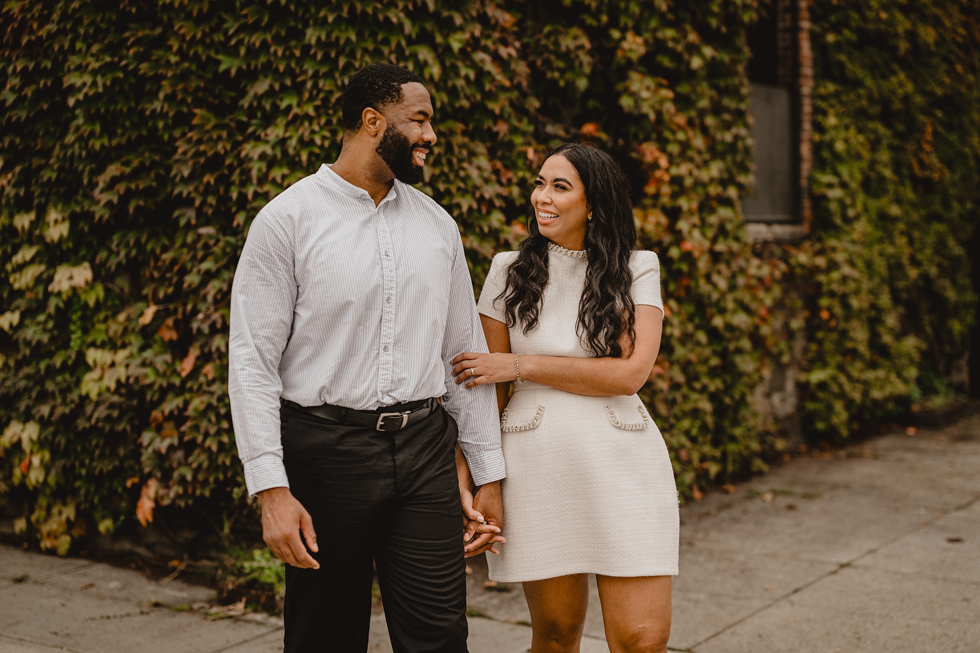 couple smiles and walks together outside Long Island City venue The Foundry on their Long Island Engagement Session