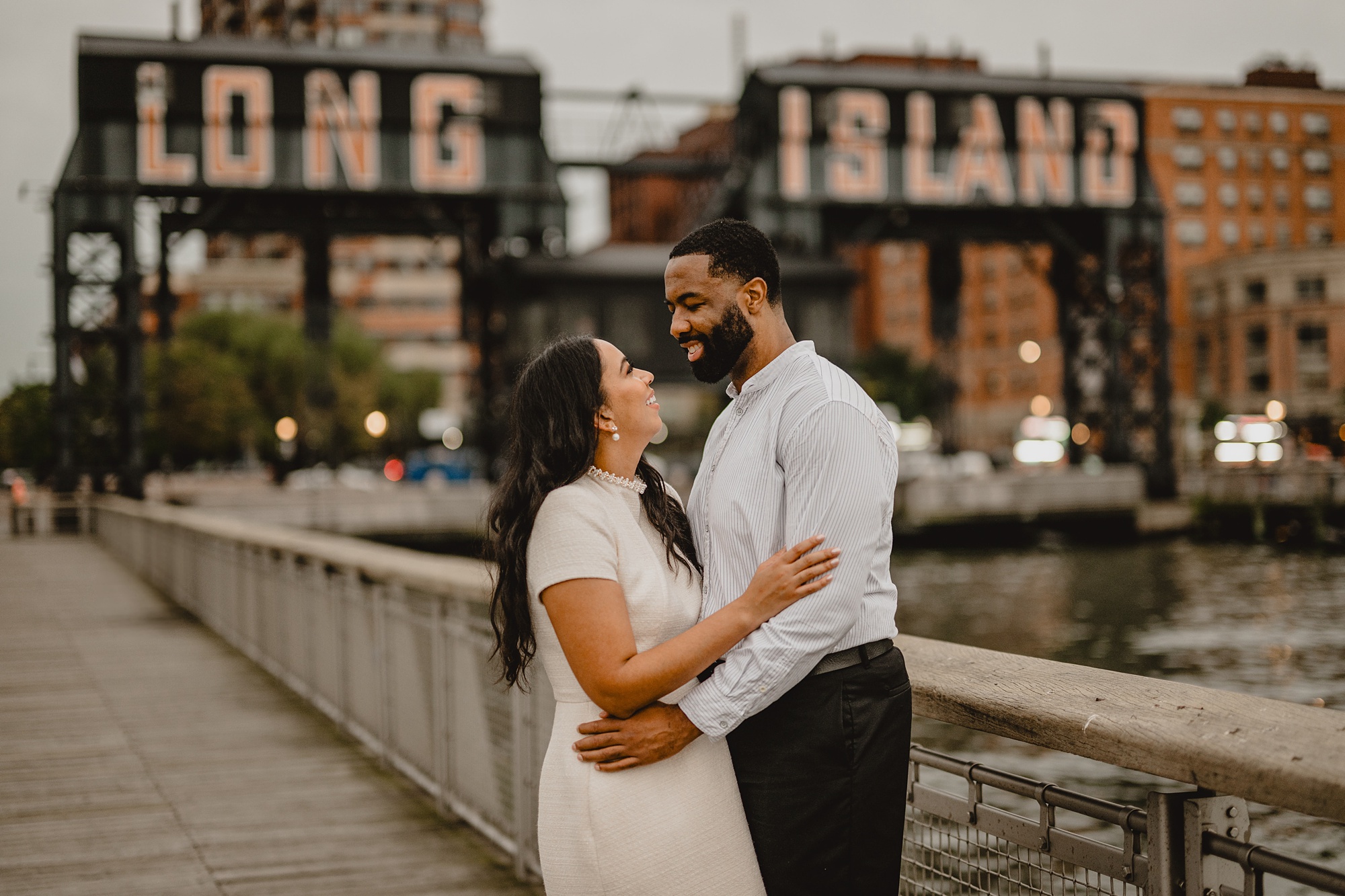 couple hugs in front of Long Island City buildings at Gantry State Park Plaza