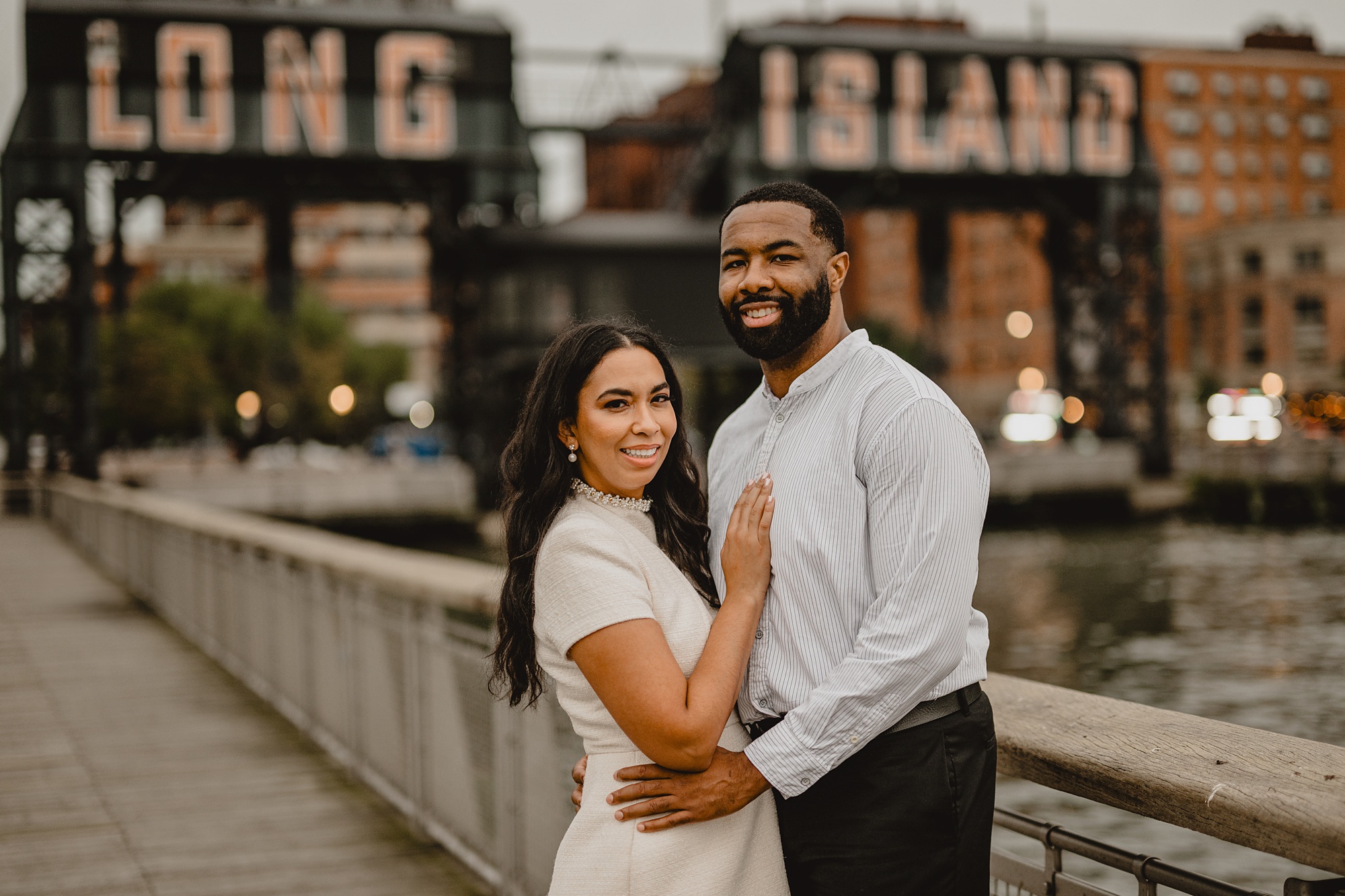 couple hugs in front of Long Island City buildings at Gantry State Park Plaza