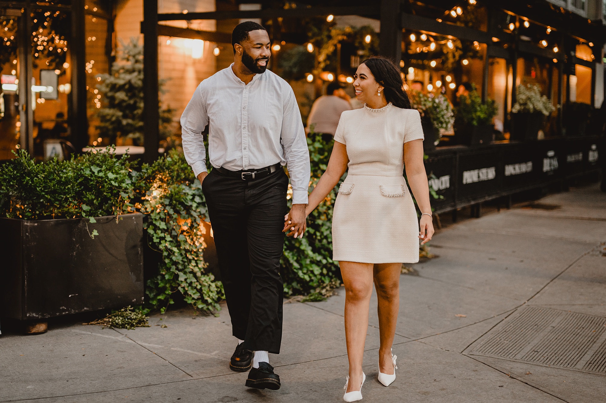 couple holds hands walking down sidewalk outside American Brass