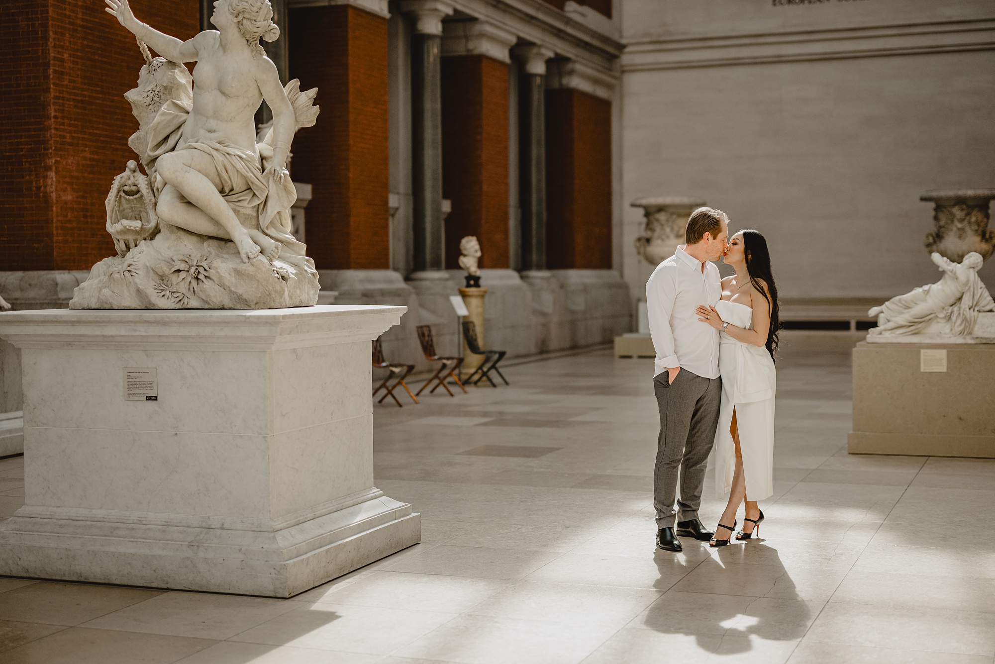 couple snuggles together by marble statue inside the Met Museum