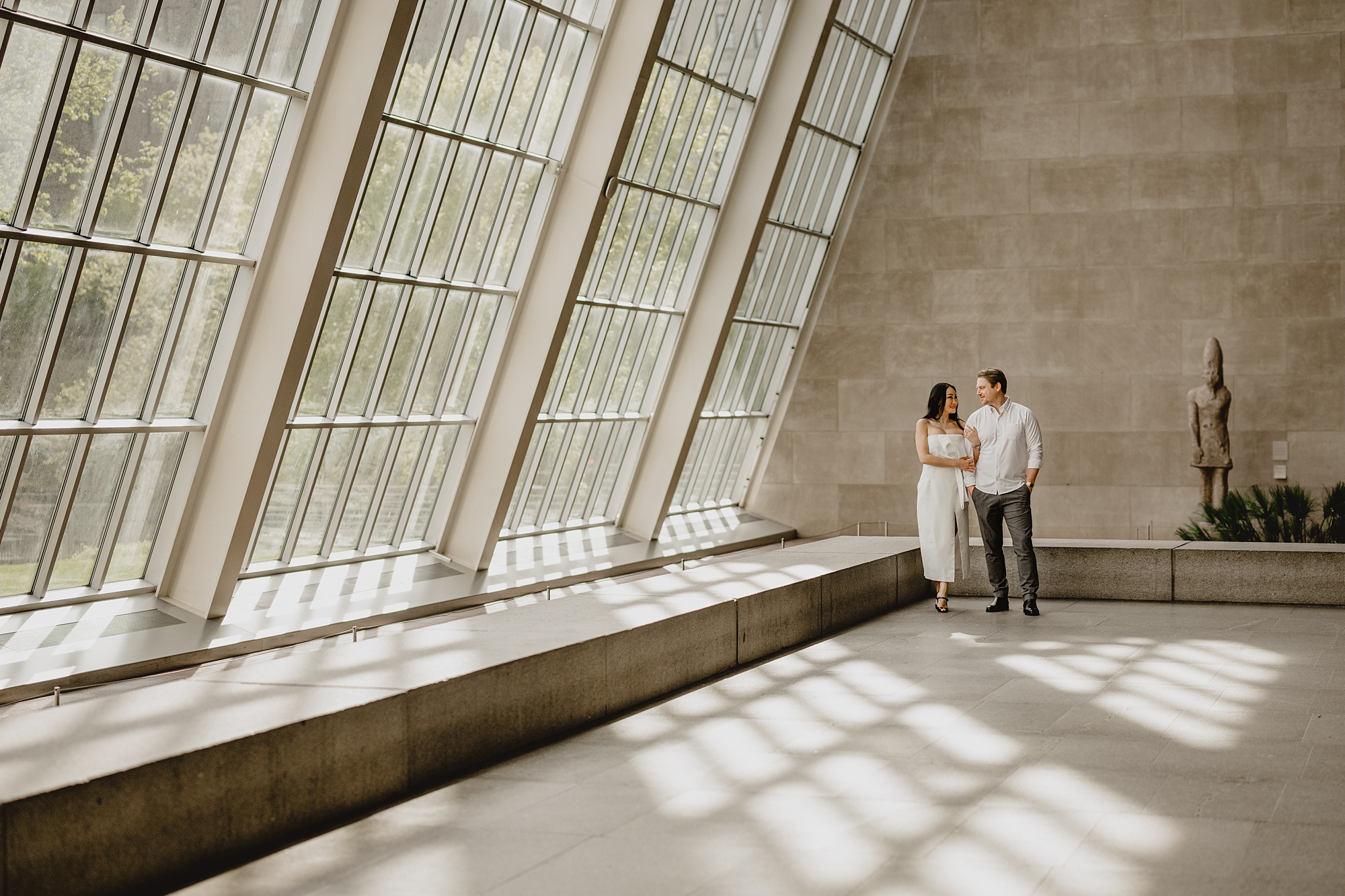man and woman pose by large wall of windows inside the Met Museum