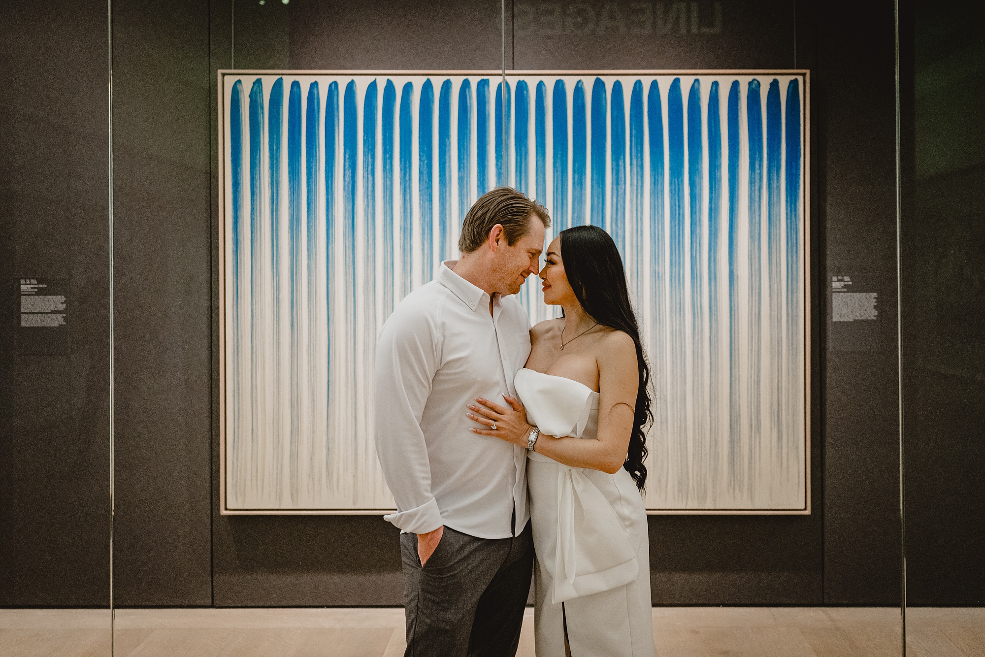 engaged couple hugs touching noses in front of blue and white artwork in NYC museum 