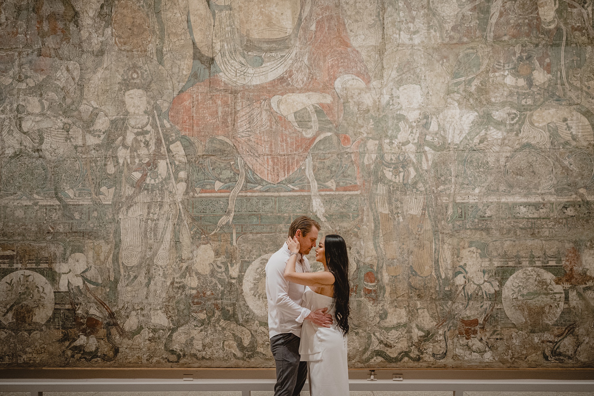 man and woman hug in front of tapestry inside NYC museum 