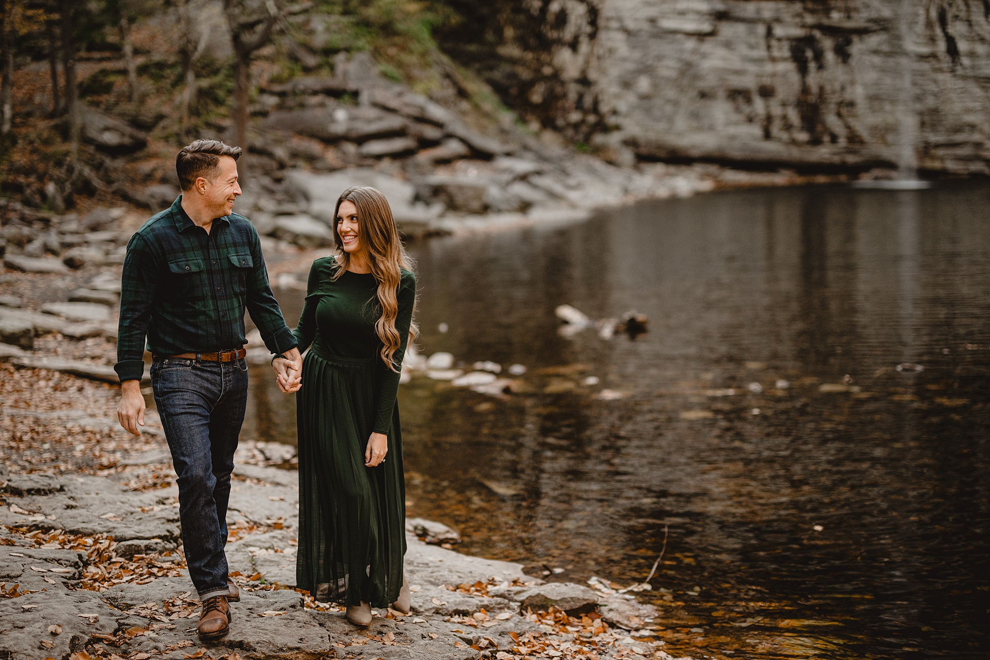 couple holds hands walking along Lake Minnewaska during engagement photos