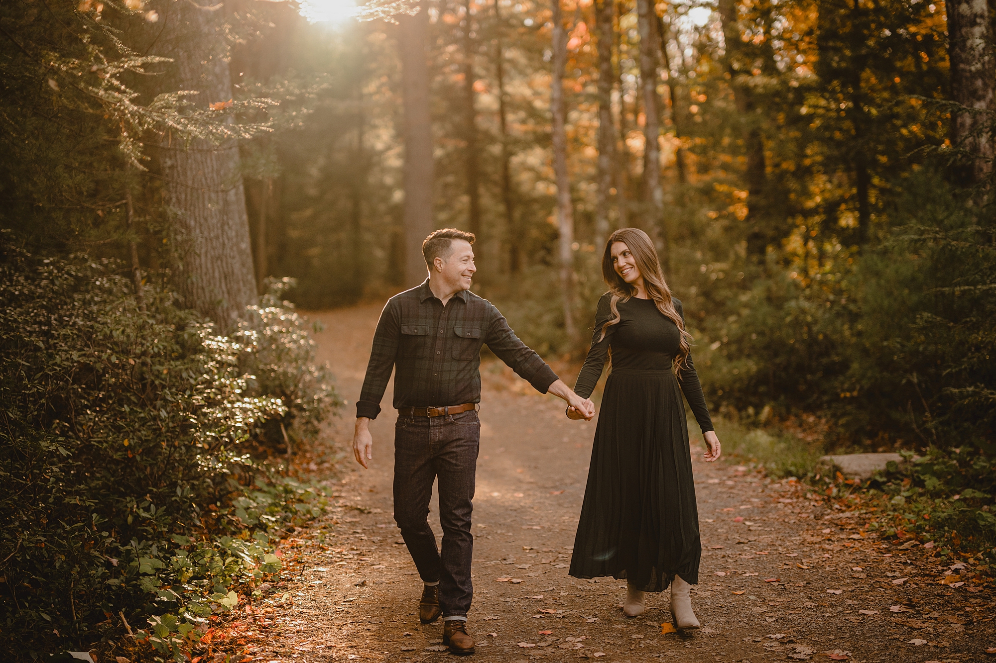 engaged couple holds hands walking down forest path at Lake Minnewaska