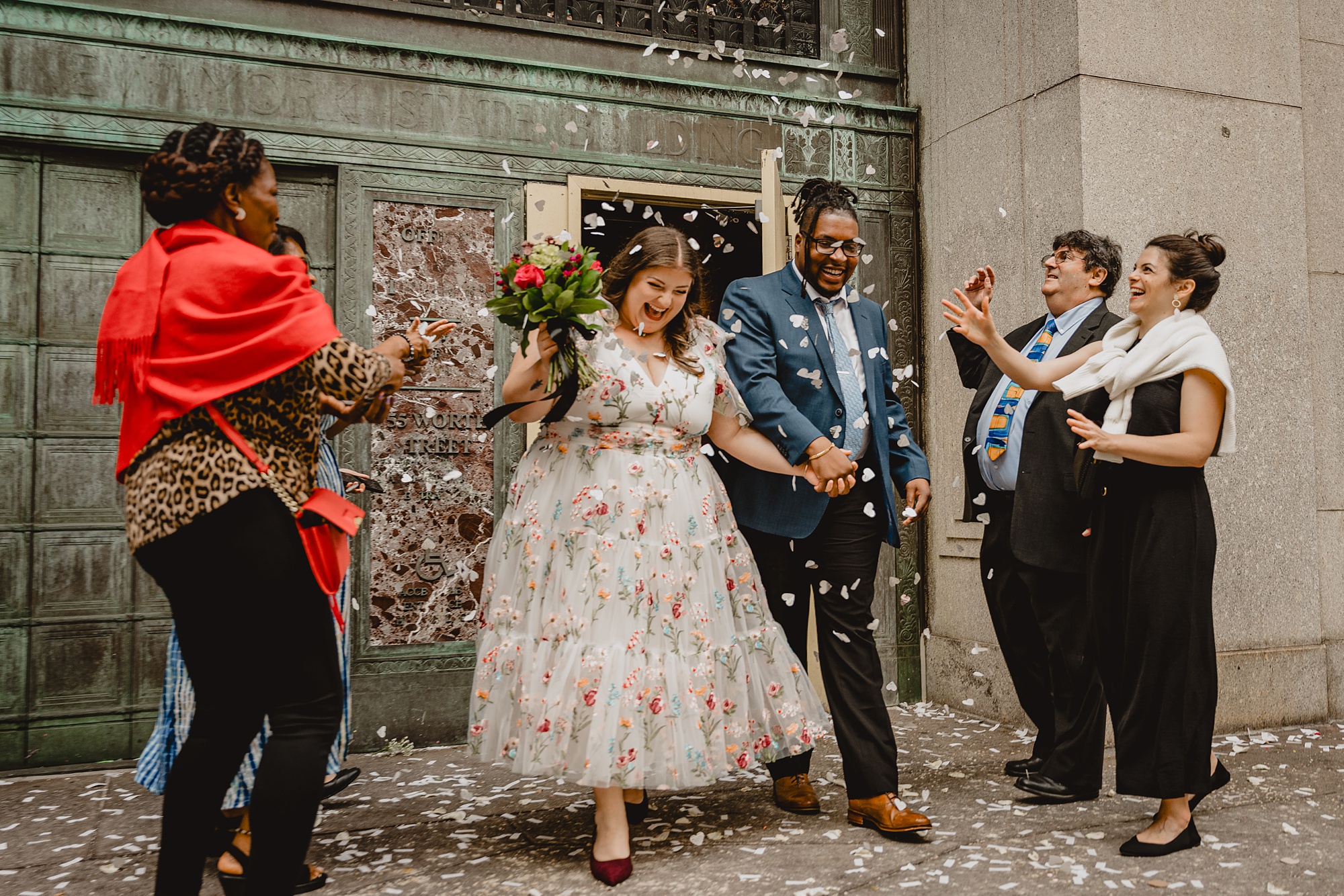 couple holds hands walking through confetti during NYC elopement at City Hall