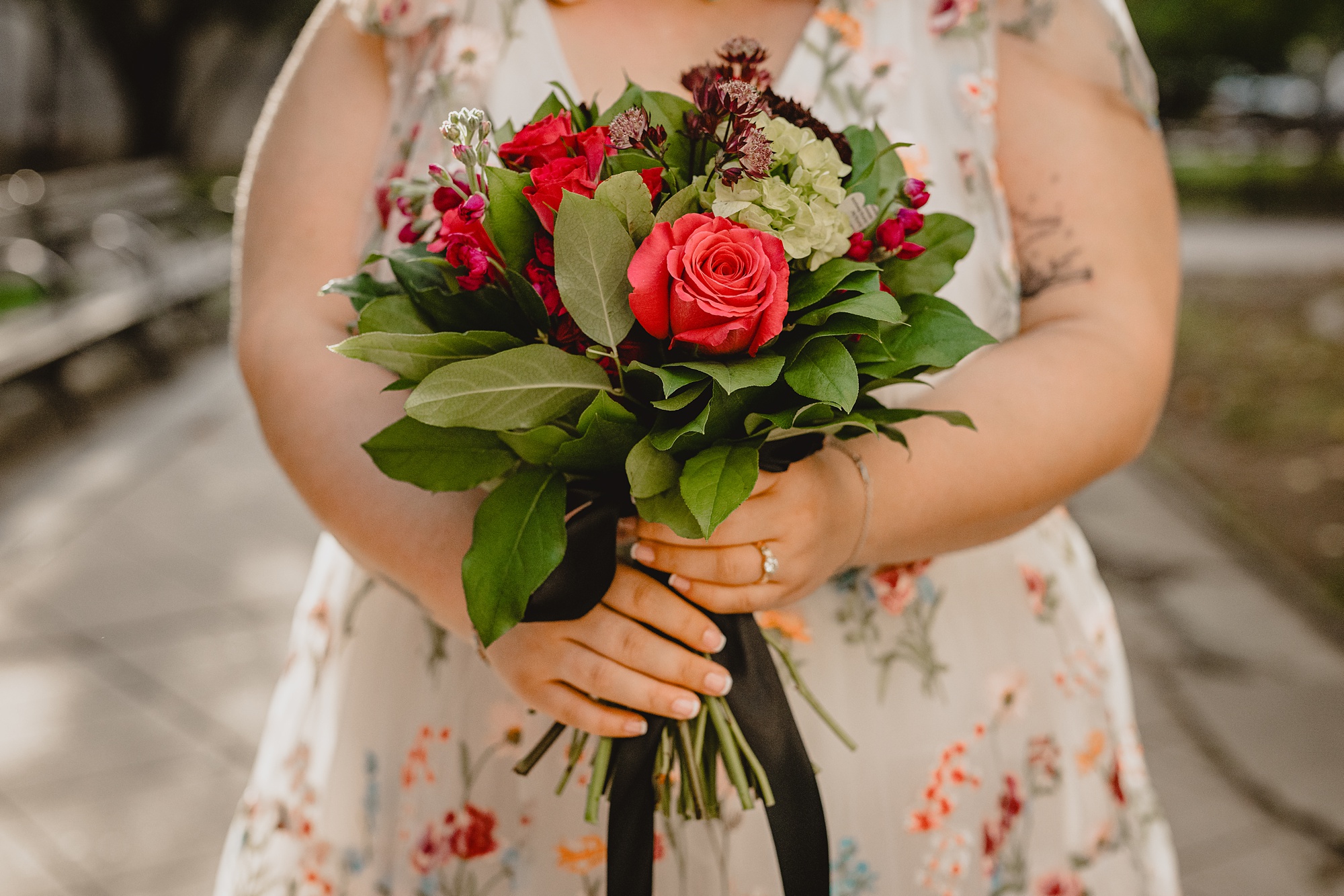 bride holds bouquet of red roses and green flowers in wedding gown embroidered with flowers
