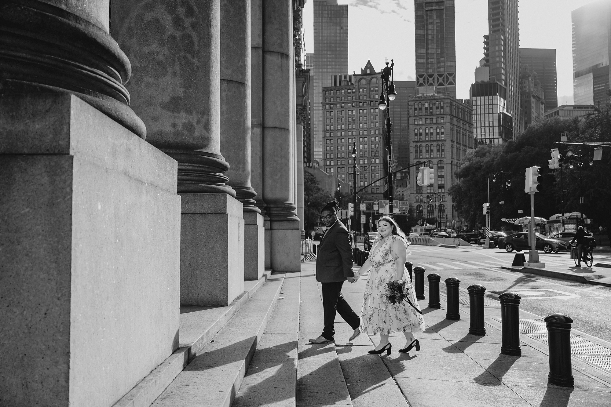 bride and groom hold hands walking up steps outside NYC City Hall