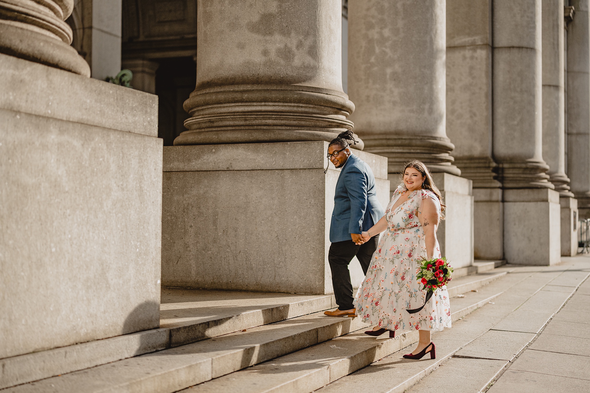 groom leads bride up stairs outside NYC City Hall