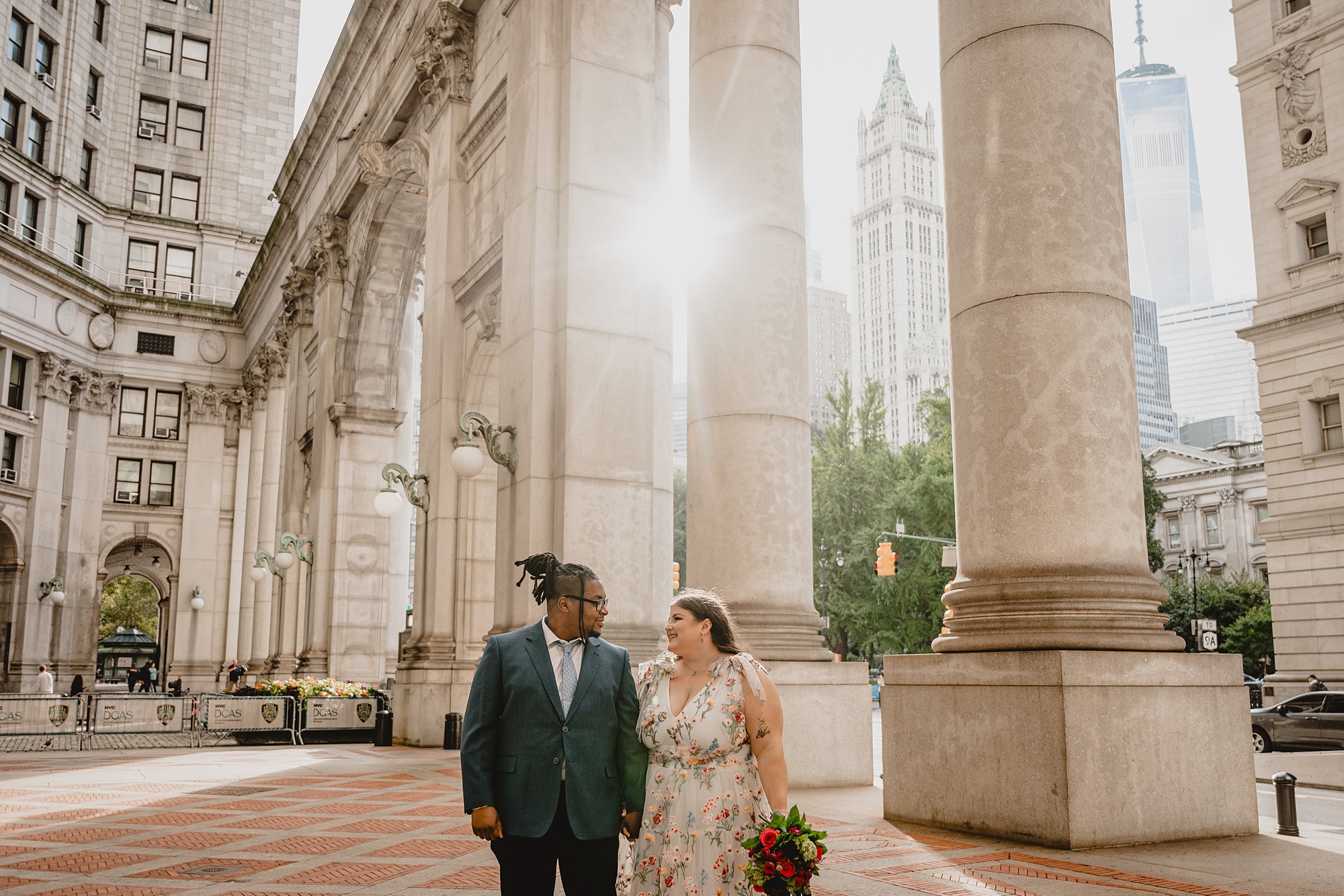 bride and groom hold hands walking between marble columns at NYC City Hall