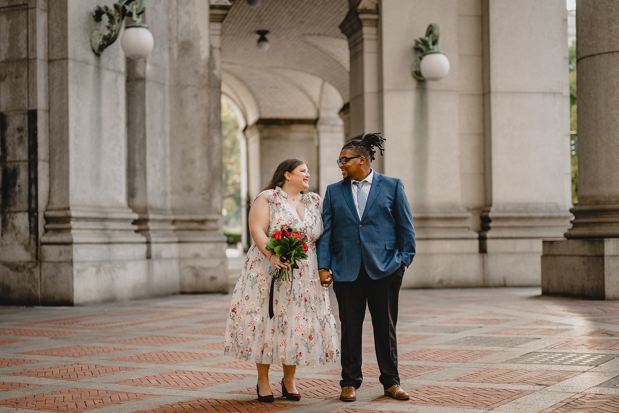 bride and groom hold hands standing together on brick patio of NYC City Hall