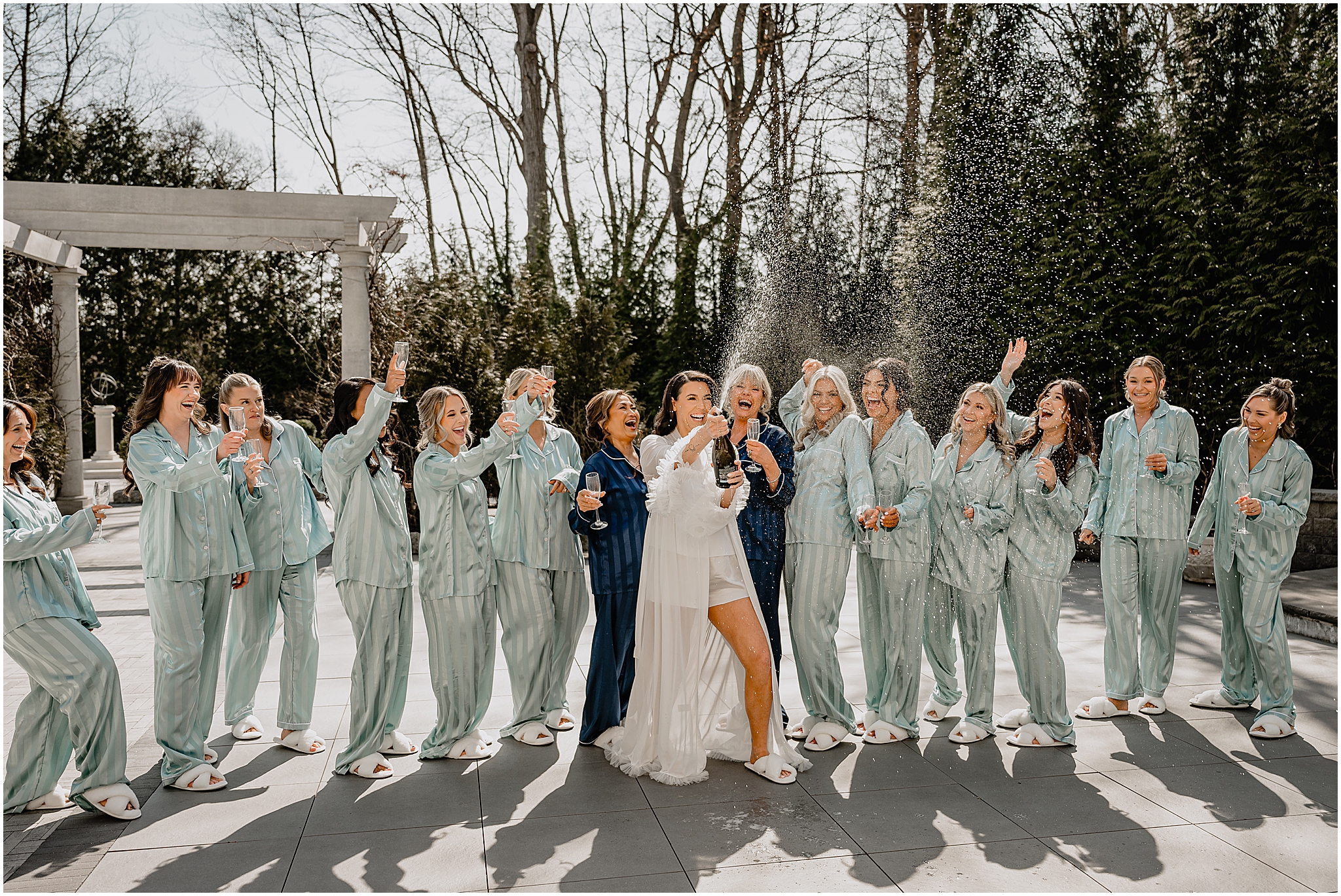 bride pops champagne with bridesmaids in matching pajamas outside the Estate at Florentine Gardens