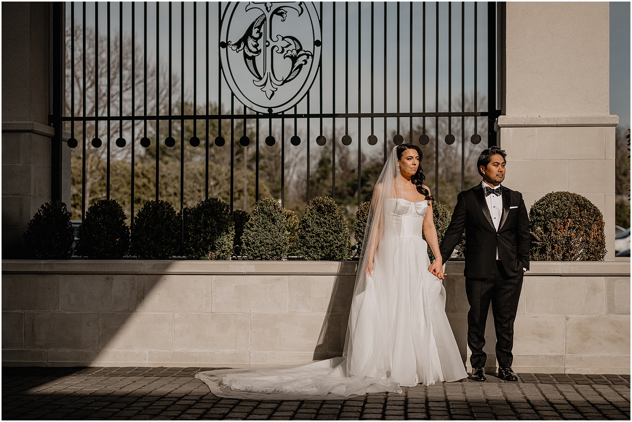 newlyweds hold hands in front of black fence at the Estate at Florentine Gardens