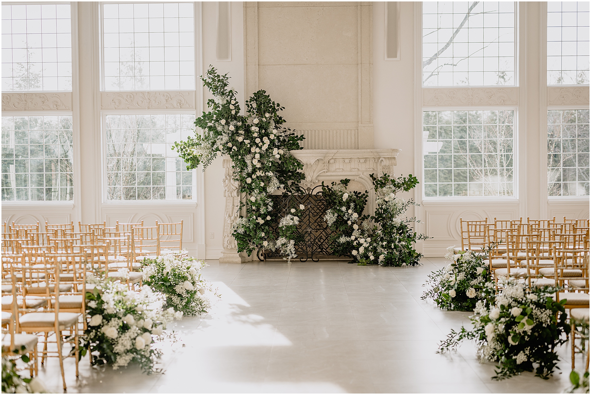 ceremony site by fireplace lined by white flowers next to gold chivari chairs inside the Estate at Florentine Gardens
