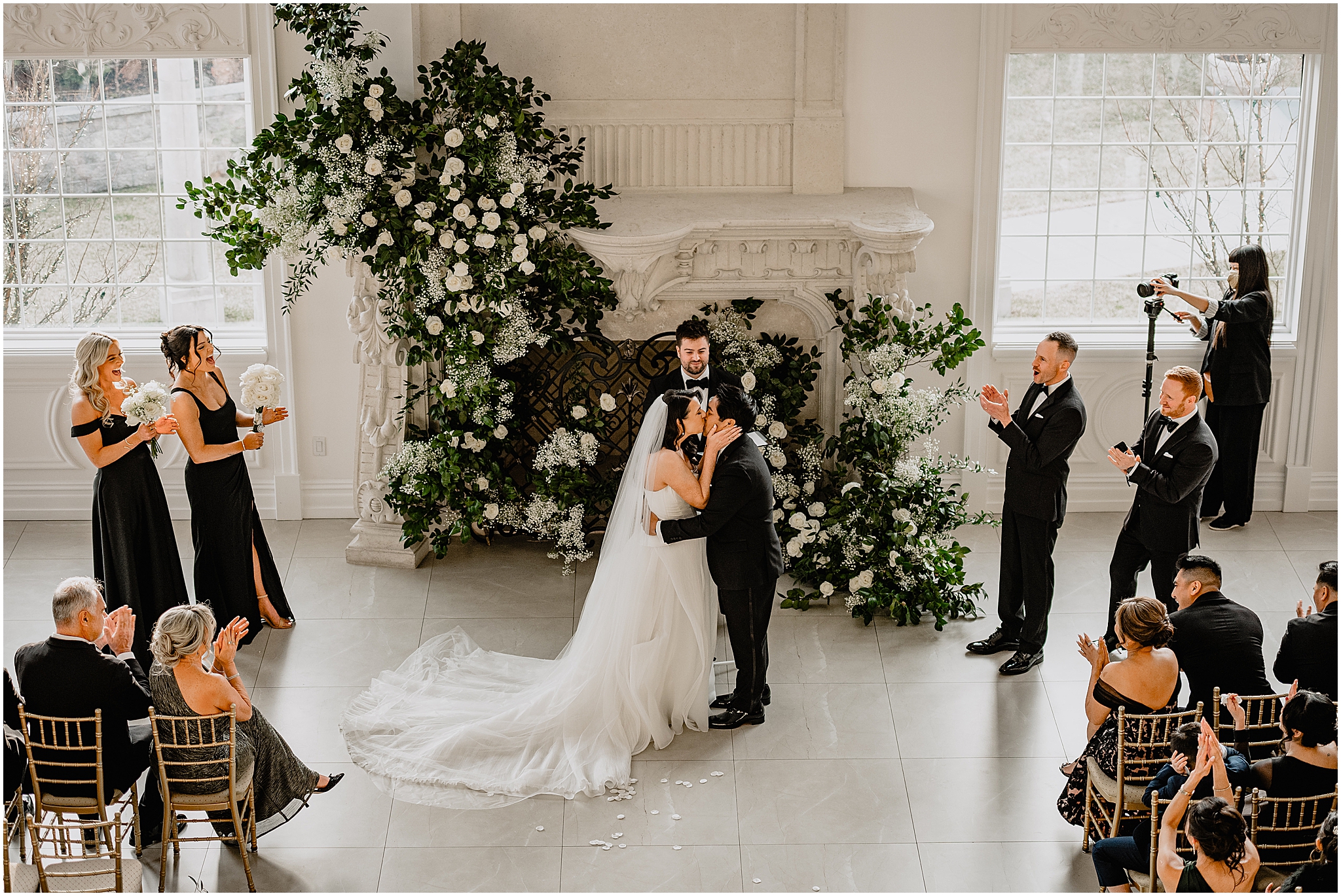 newlyweds kiss by fireplace covered in white roses and baby's breath at the Estate at Florentine Gardens